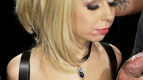 Shackled Blonde In Leather Suit Is Served Two Cocks